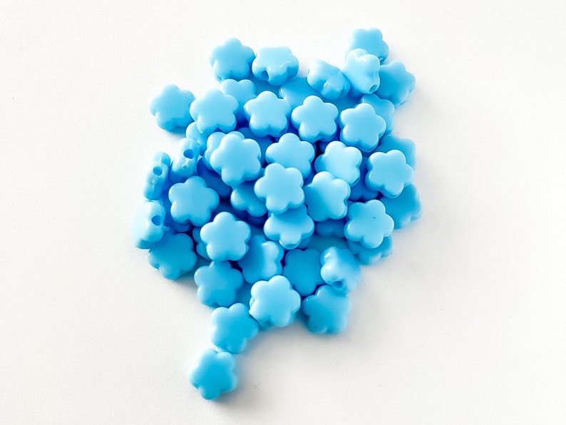 K&ouml;nnte beinhalten: Ein Haufen hellblauer, blumenf&ouml;rmiger Perlen. Die Perlen sind aus Kunststoff und haben eine glatte Oberfl&auml;che.