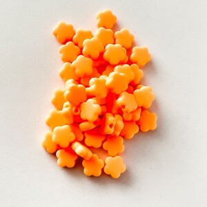 K&ouml;nnte beinhalten: Ein Haufen kleiner, leuchtend orangefarbener Perlen in Blumenform.