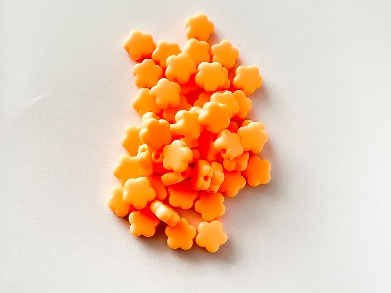 K&ouml;nnte beinhalten: Ein Haufen kleiner, leuchtend orangefarbener Perlen in Blumenform.