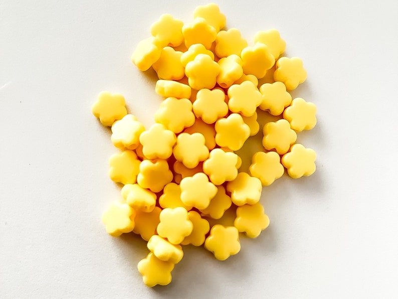 K&ouml;nnte beinhalten: Ein Haufen gelber, blumenf&ouml;rmiger Silikonperlen. Diese Perlen eignen sich perfekt f&uuml;r die Herstellung von Schmuck oder anderen Bastelarbeiten.