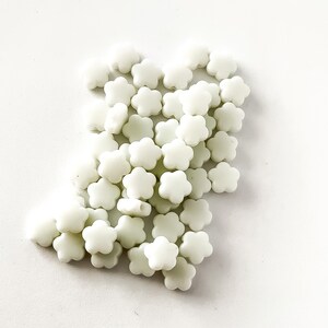 K&ouml;nnte beinhalten: Ein Haufen wei&szlig;er, blumenf&ouml;rmiger Perlen. Die Perlen sind aus Kunststoff und haben eine matte Oberfl&auml;che.