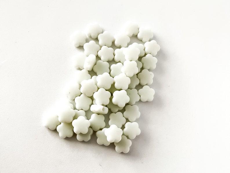 K&ouml;nnte beinhalten: Ein Haufen wei&szlig;er, blumenf&ouml;rmiger Perlen. Die Perlen sind aus Kunststoff und haben eine matte Oberfl&auml;che.