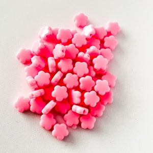 K&ouml;nnte beinhalten: Ein Haufen rosa Plastikperlen in Blumenform. Die Perlen sind klein und haben ein Loch in der Mitte zum Auf f&auml;deln.