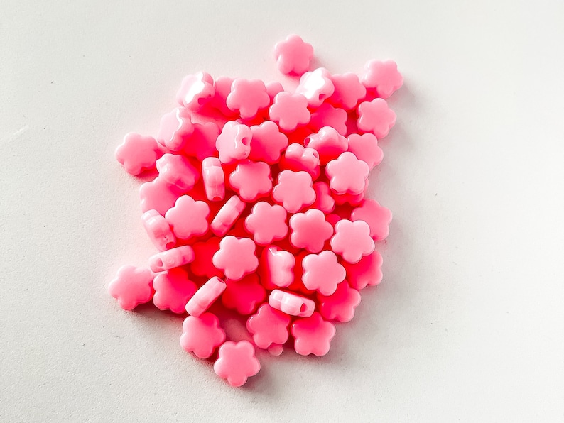 K&ouml;nnte beinhalten: Ein Haufen rosa Plastikperlen in Blumenform. Die Perlen sind klein und haben ein Loch in der Mitte zum Auf f&auml;deln.