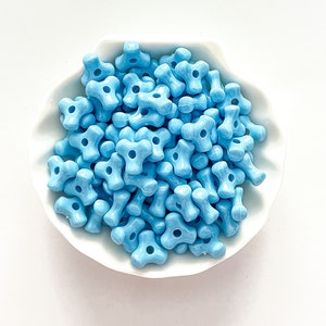 May include: A bowl filled with light blue plastic beads. The beads are shaped like a four-pointed star with a hole in the centre.