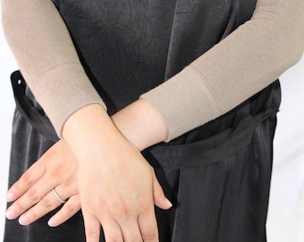 May include: A black dress with short sleeves and a cinched waist. The sleeves are covered with beige arm warmers. The person is wearing a silver ring on their finger. The dress has a textured appearance.