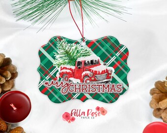 Può includere: Ornamento natalizio con un camion rosso vintage che trasporta un albero di Natale innevato. L'ornamento ha uno sfondo a quadri verde e rosso e le parole "Merry Christmas".