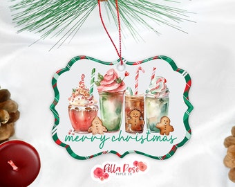 Puede incluir: Un adorno navideño con un diseño de acuarela que presenta cuatro bebidas festivas con crema batida, bastones de caramelo y hombres de jengibre. El adorno tiene un borde a cuadros verde y rojo y las palabras "merry christmas".