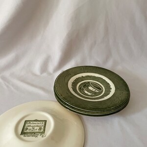 Può includere: Set di quattro piattini in ceramica verde e bianca con un motivo a venature del legno e un design a barile. Il fondo di un piattino ha il testo "Colonial Homestead by Regal" in un quadrato verde.