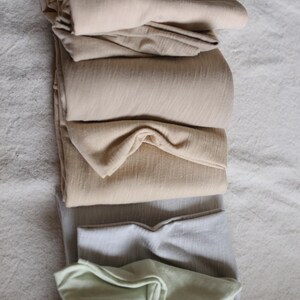 May include: A stack of folded fabric in various shades of beige, gray, and green. The fabric is soft and smooth, and it appears to be made of a natural material.