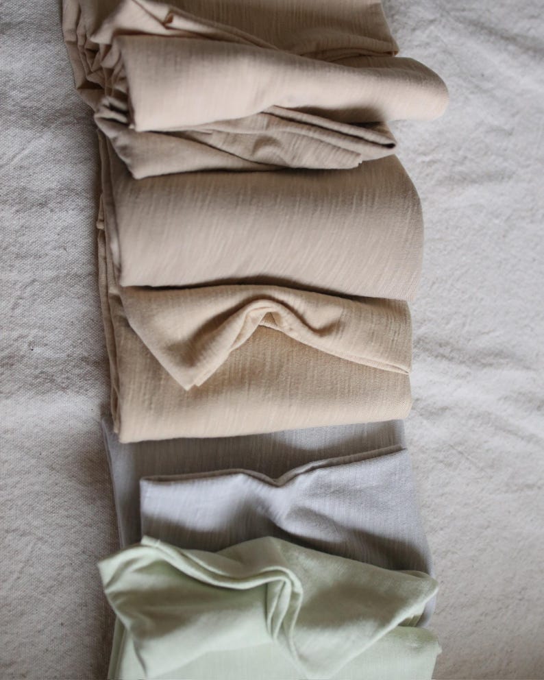 May include: A stack of folded fabric in various shades of beige, gray, and green. The fabric is soft and smooth, and it appears to be made of a natural material.