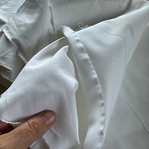 High-resolution image of 16 oz heavyweight cotton twill fabric in undyed, natural state. The tightly woven twill pattern and soft, yet sturdy feel highlight its quality. Made from 100% cotton and prepared for dyeing (PFD), this fabric is perfect for creating workwear garments, utility clothing, and durable home décor items. Shown draped and folded to showcase thickness, texture, and sewing potential for professional or hobbyist use.