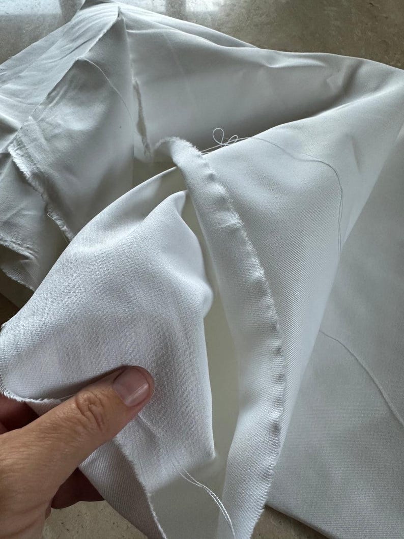 High-resolution image of 16 oz heavyweight cotton twill fabric in undyed, natural state. The tightly woven twill pattern and soft, yet sturdy feel highlight its quality. Made from 100% cotton and prepared for dyeing (PFD), this fabric is perfect for creating workwear garments, utility clothing, and durable home décor items. Shown draped and folded to showcase thickness, texture, and sewing potential for professional or hobbyist use.