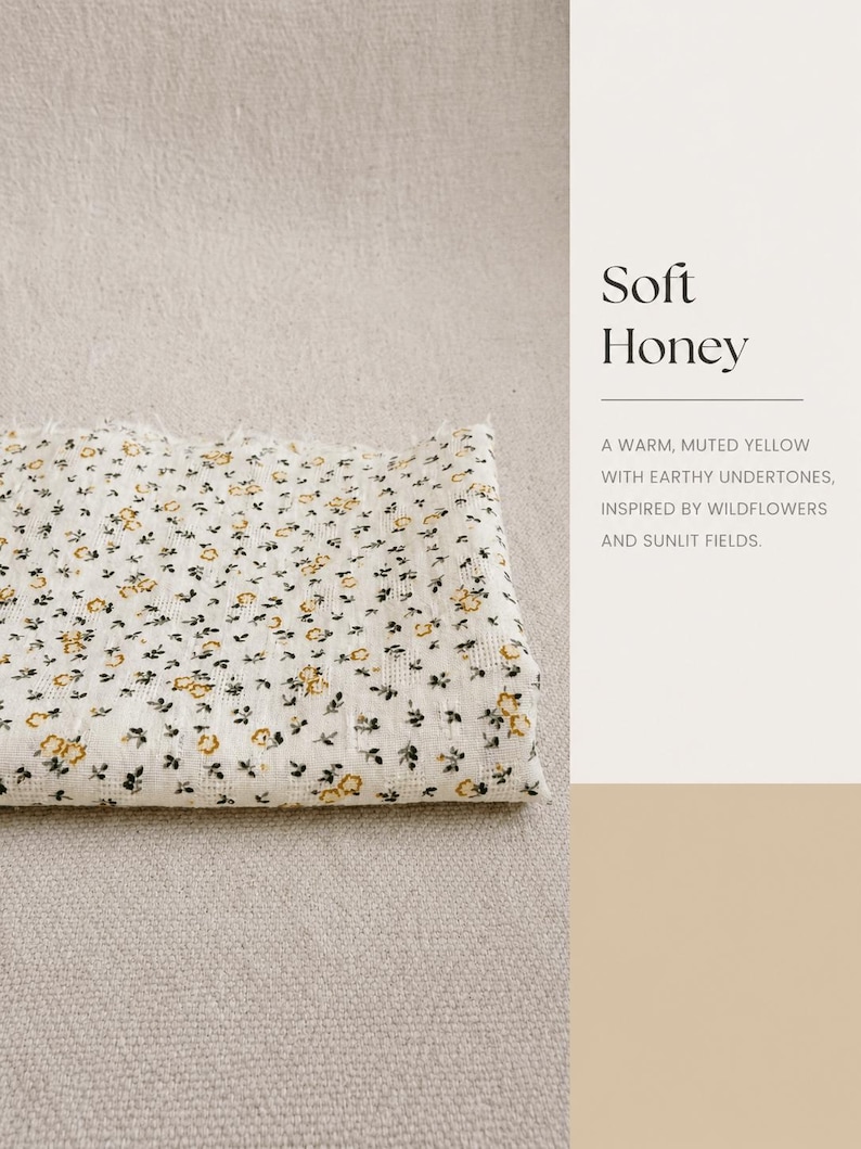 May include: A folded piece of off-white fabric featuring a small-scale floral pattern with yellow blossoms and dark green leaves. The text on the right side reads Soft Honey, A WARM, MUTED YELLOW WITH EARTHY UNDERTONES, INSPIRED BY WILDFLOWERS AND SUNLIT FIELDS.