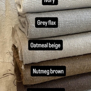 May include: A stack of fabric samples in various neutral colors. The colors include ivory, grey flax, oatmeal beige, nutmeg brown, and espresso brown. Each fabric swatch has a woven texture, and the color names are displayed on black labels.