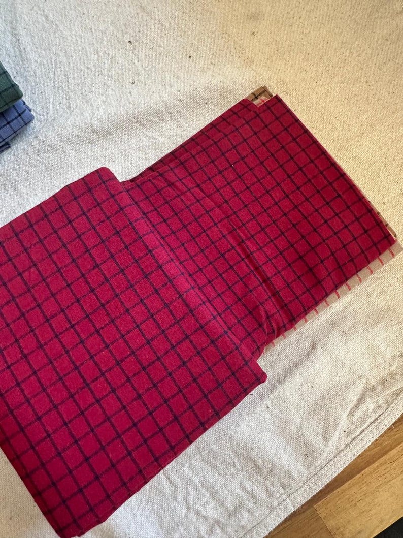 Brushed cotton grid plaid fabric draped on a sewing table, with scissors and thread nearby. The fabric’s clean lines and soft feel suggest its readiness for quilting or garment-making. Woven design adds depth while the brushed cotton enhances comfort. A dream material for home sewers, designers, and textile lovers seeking quality.