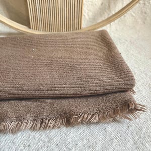 Heavy cotton sweater knit fabric draped over a tabletop, highlighting the natural folds and stretch of the ribbed texture. This thick knit is designed for crafting warm apparel such as slouchy beanies, oversized sweaters, and lounge sets. The neutral shade and quality weave make it a versatile textile for cold-season fashion.