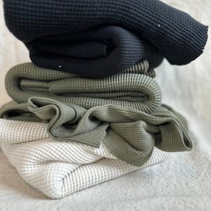 Premium heavy cotton waffle knit fabric shown with a thick textured surface and classic waffle pattern. This high-quality cotton knit fabric is soft, breathable, and substantial, making it ideal for sewing hoodies, sweaters, joggers, loungewear, baby clothing, and cozy blankets. The waffle texture adds dimension and warmth while maintaining flexibility and comfort. Fabric is sold by the half yard and is suitable for both apparel sewing and home projects.