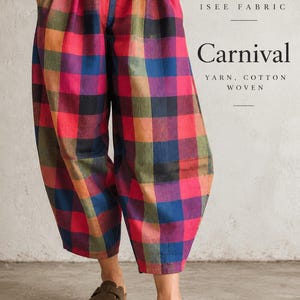 May include: Loose-fitting trousers featuring a vibrant multicolored plaid pattern in shades of red, blue, green, and black. The text ISEE FABRIC Carnival YARN, COTTON WOVEN is visible on the right side. The trousers have an elastic waistband.