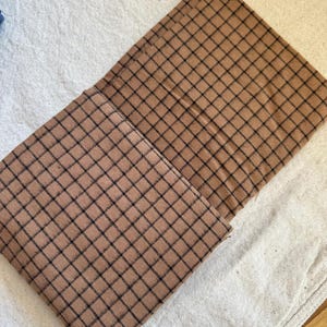 Fabric rolled loosely on a cutting mat, ready for DIY cutting and patterning. Brushed cotton grid plaid fabric features a soft, cozy feel and woven plaid details. Perfect for a wide range of projects including baby blankets, clothing, and decorative pieces. The photo captures the tactile quality and versatility of this textile.