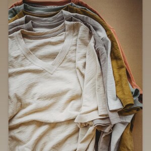May include: A stack of folded, light-colored t-shirts in various shades of beige, gray, and brown. The shirts are made of a slub fabric, which gives them a textured look. The text "I love our slub fabric and this is such a pretty stack! Iseefabric.com" is at the top of the image. The text "@the_makings_of_a_miracle" is at the bottom of the image.