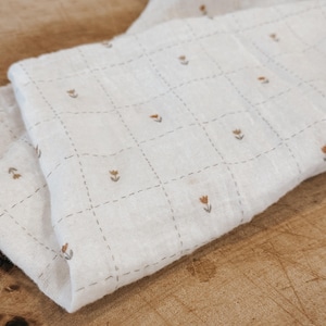 Lightweight salt air cotton gauze fabric shown in soft natural tones with a slightly crinkled texture. This breathable double gauze cotton has an airy weave and soft drape, perfect for baby blankets, summer garments, and layering pieces. Fabric is displayed in folds to highlight texture and movement, with a clean neutral aesthetic ideal for modern sewing projects. Natural cotton fibers create a soft, skin-friendly fabric suitable for apparel and accessories.