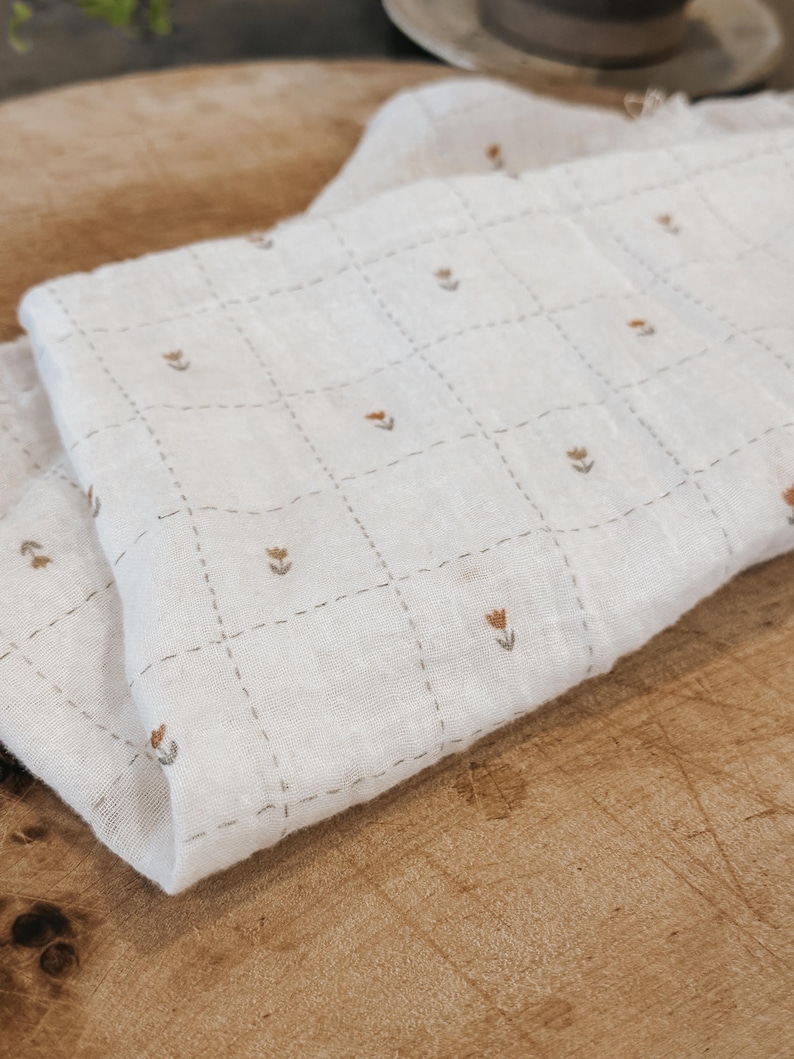 Lightweight salt air cotton gauze fabric shown in soft natural tones with a slightly crinkled texture. This breathable double gauze cotton has an airy weave and soft drape, perfect for baby blankets, summer garments, and layering pieces. Fabric is displayed in folds to highlight texture and movement, with a clean neutral aesthetic ideal for modern sewing projects. Natural cotton fibers create a soft, skin-friendly fabric suitable for apparel and accessories.