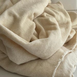 May include: A folded, cream-colored towel with a textured surface. The towel is made of a soft material and has a frayed edge. The towel is likely used for bathing or drying.