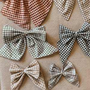 May include: Six different sizes of gingham fabric bows in various colours, including brown, tan, green, and black. The bows are arranged on a beige surface. The text "COTTAGE BOW PATTERN" and "6 sizes/ 1 file" is displayed below the bows.