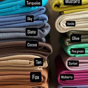 May include: Stacks of folded fabric in various colors, including Poppy, Turquoise, Sky, Slate, Cocoa, Tan, Fox, Rust, Mustard, Vanilla, Olive, Pea green, Sorbet, Mulberry, and Wisteria. Each color is labeled with a black rectangle.