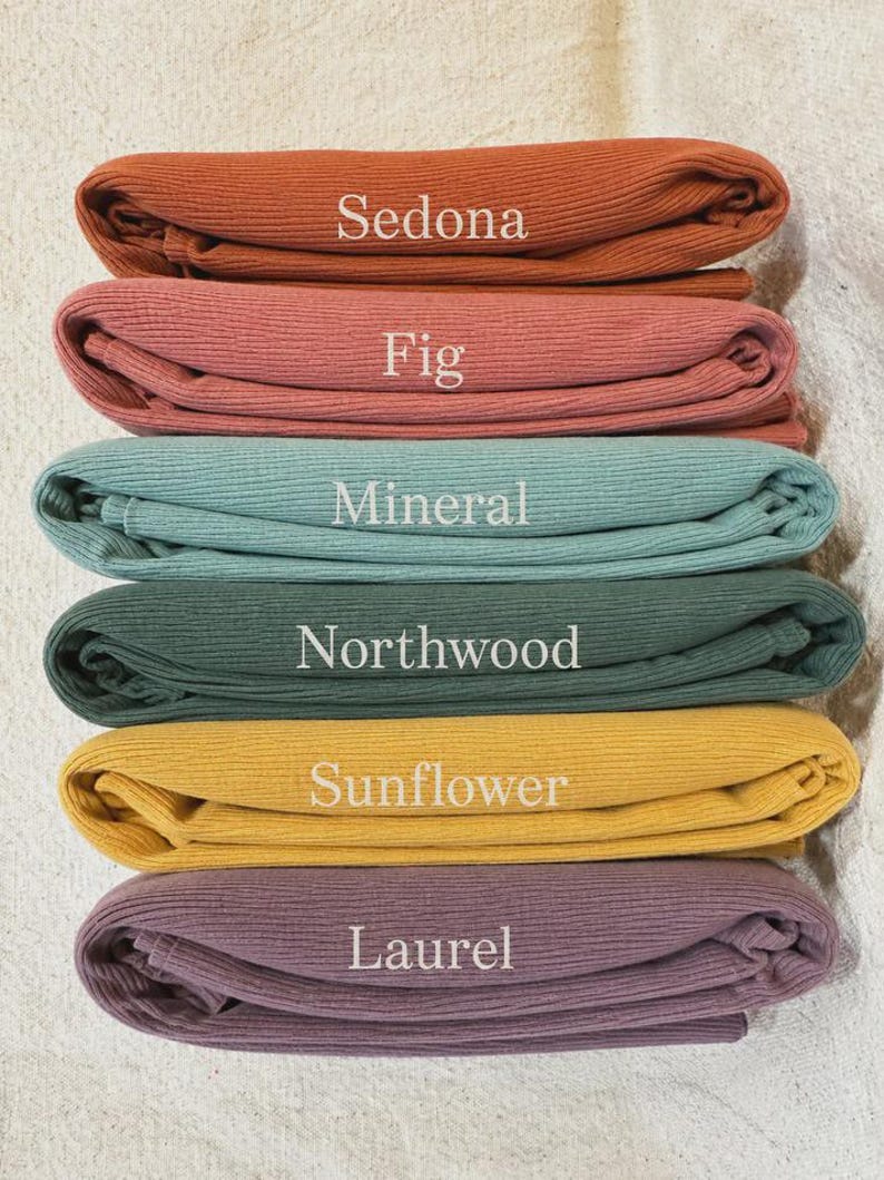 May include: A stack of six folded ribbed fabric pieces in various colors. The colors are labeled with white text as Sedona, Fig, Mineral, Northwood, Sunflower, and Laurel. Each piece of fabric features a consistent vertical ribbed texture.