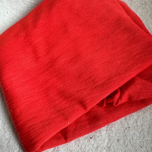May include: A folded piece of bright red fabric, possibly a scarf or clothing item, with a textured surface. The fabric is neatly folded, highlighting its vibrant colour and potential use in fashion or textiles.