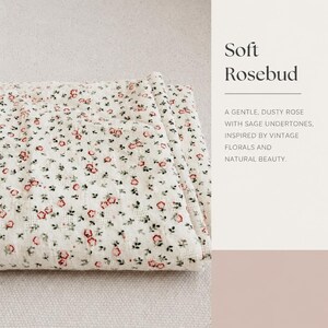 May include: A folded white fabric featuring a repeating pattern of small red rosebuds and green leaves. The text on the right side reads: Soft Rosebud. A GENTLE, DUSTY ROSE WITH SAGE UNDERTONES, INSPIRED BY VINTAGE FLORALS AND NATURAL BEAUTY.