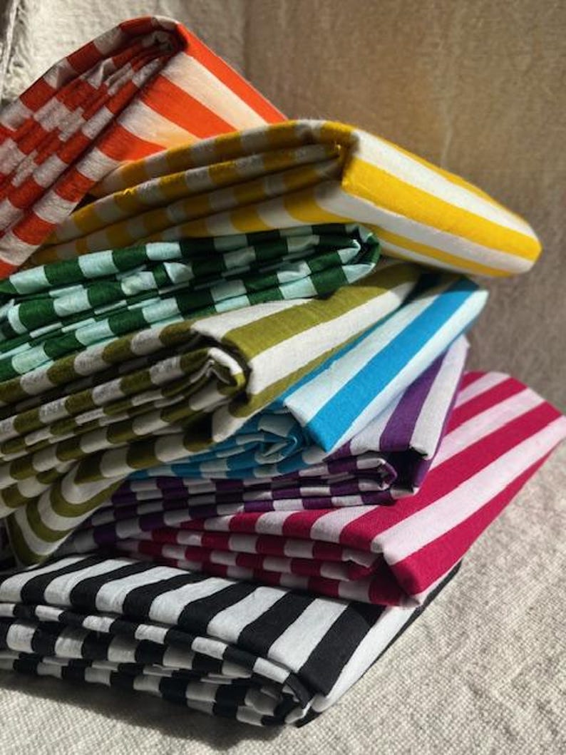 "Draped Carnival Cotton fabric, highlighting its smooth, tightly woven texture and festive patterns. Great for sewing stylish apparel, lightweight curtains, and decorative accents. The natural cotton fibers enhance breathability, ensuring a comfortable feel."