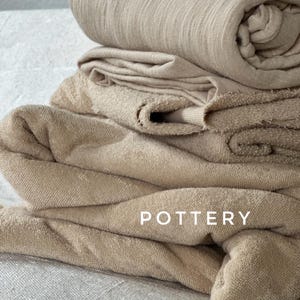 May include: A stack of beige fabric towels with the word "POTTERY" printed on the bottom towel.
