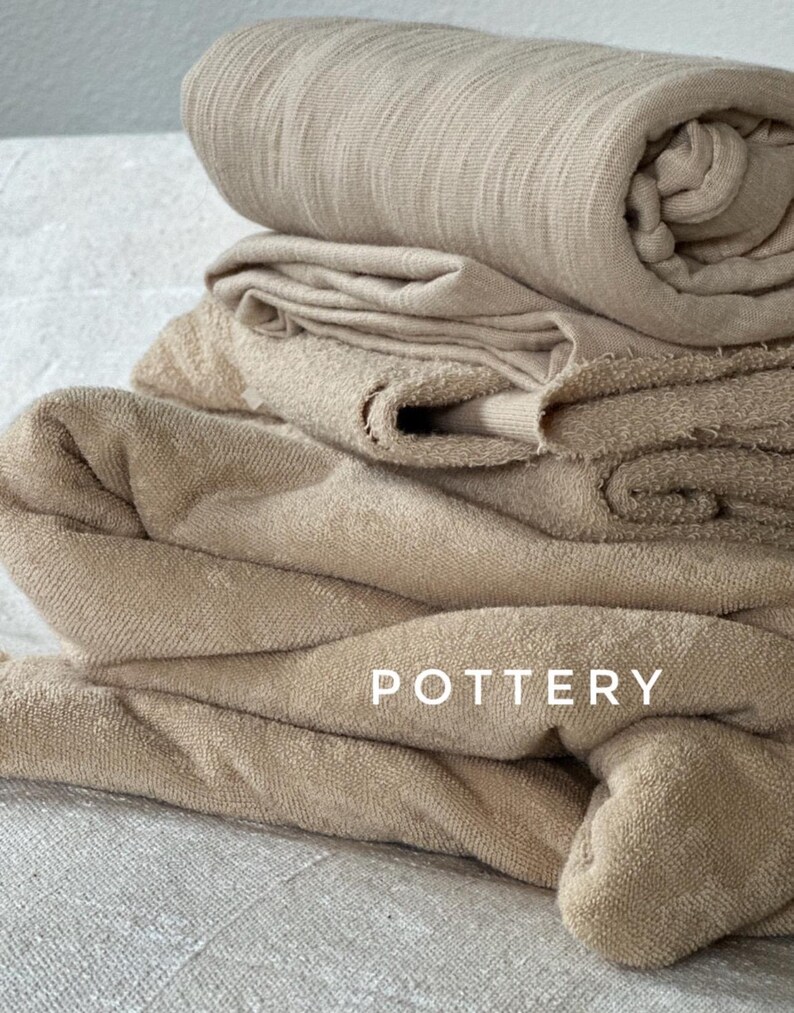 May include: A stack of beige fabric towels with the word "POTTERY" printed on the bottom towel.