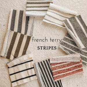 May include: Assortment of striped fabric swatches in various colors, including brown, white, black, and red. The fabric is described as "french terry stripes".