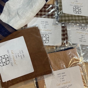 以下が含まれることがあります： さまざまな色のリネン生地の正方形のアソートメントで、透明なプラスチックで包装されています。 各パッケージには、12.7cm x 12.7cmの正方形が9個入っており、「100% LINEN」と「Get creative!」の文字がラベルに印刷されています。