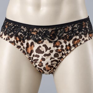 May include: Briefs featuring a tan, brown, and black leopard print pattern. The waistband is accented with a wide band of black floral lace trim. The fabric has a smooth finish and the leg openings are finished with a simple stitched hem.