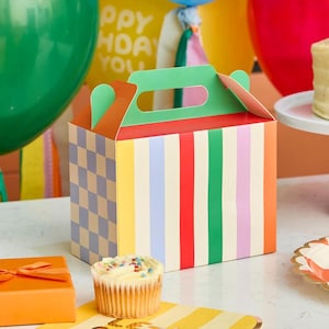 May include: A rectangular cardboard party favour box with a handle, featuring a side panel with a light blue and beige checkerboard pattern and a front panel with vertical stripes in yellow, light blue, red, green, and light purple colours.