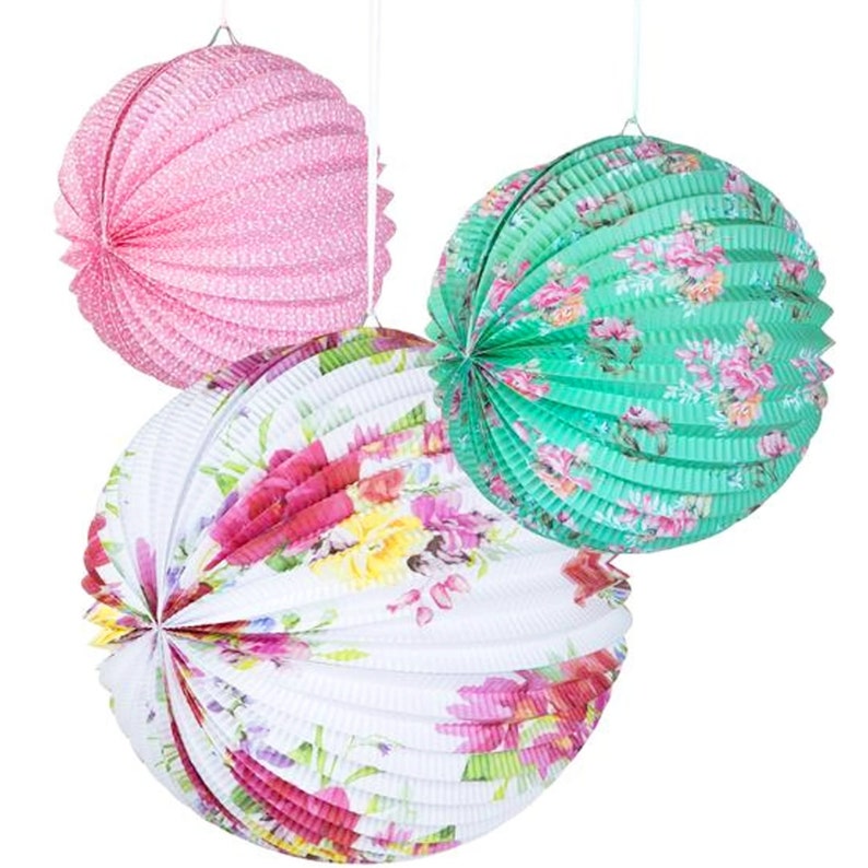 May include: Three round paper lanterns with floral patterns. The lanterns are pink, green, and white with a white background and colorful floral designs.