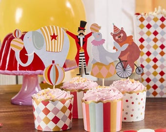 Könnte beinhalten: Vier rosa glasierte Cupcakes, verziert mit bunten, zirkusartigen Toppern. Die Topper zeigen einen Elefanten, eine Robbe, die einen Ball balanciert, einen Zirkusdirektor und einen Bären, der ein Einrad fährt. Die Cupcakes sind in rot-weiß-goldenen gestreiften und gepunkteten Cupcake-Förmchen.