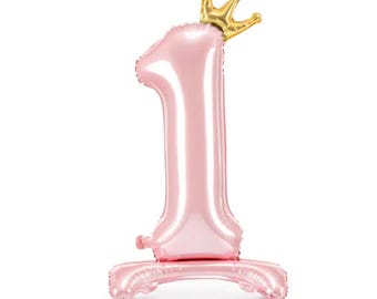 May include: A pink number one balloon with a gold crown on top. The balloon is standing on a pink base.