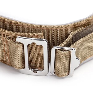 May include: Close-up of a tan nylon strap with two silver metal buckles. The strap is woven with a fine texture.