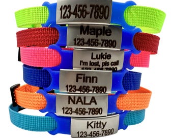 May include: A stack of colorful pet ID collars with blue silicone bases and various colored nylon straps. Each collar has a silver metal tag with a pet's name and a phone number. The text "I'm lost, pls call" is on one tag.