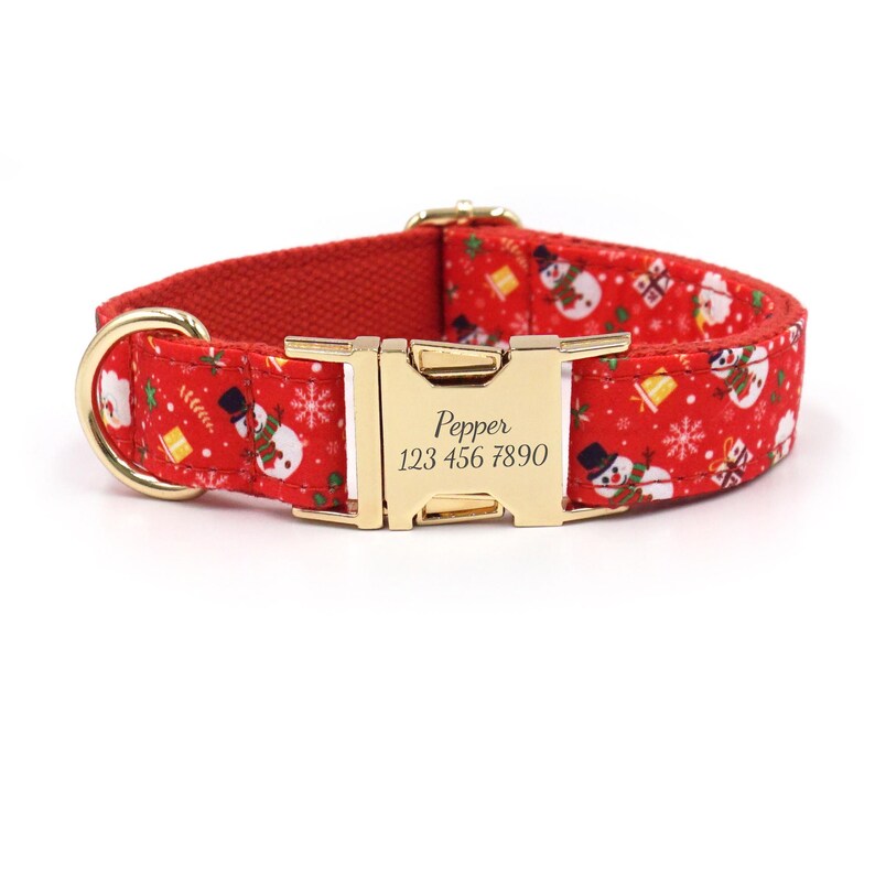 May include: Red dog collar with a gold buckle and a snowman pattern. The buckle is engraved with the text "Pepper 123 456 7890".