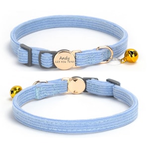 May include: Light blue cat collar with a gold-colored bell and buckle. The collar has a gray buckle and a gold-colored tag with the name "Andy" and a phone number. The collar is made of a soft, textured material.