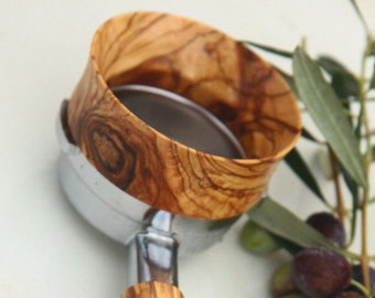 Puede incluir: Un tamper de espresso de madera con un acabado de grano de madera natural. El tamper tiene una base de metal y un mango de madera. El mango está hecho de madera de olivo y tiene un patrón de grano único.