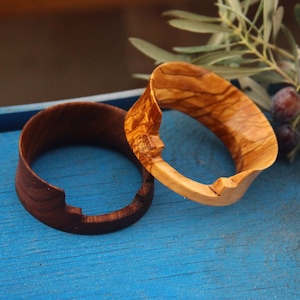 May include: Two wooden rings, one brown and one light brown with a wood grain pattern, on a blue surface.