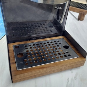以下が含まれることがあります： Gaggia Classic エスプレッソマシンのクローズアップ。マシンはステンレス鋼のトップと透明な水タンクを備えています。 ドリップトレイは木製のベースが付いたステンレス鋼です。 「Gaggia Classic」の文字が見えます。